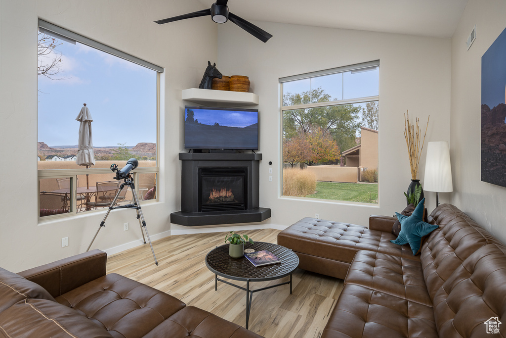 Living area with vaulted ceiling, a ceiling fan, wood finished floors, a glass covered fireplace, and visible vents