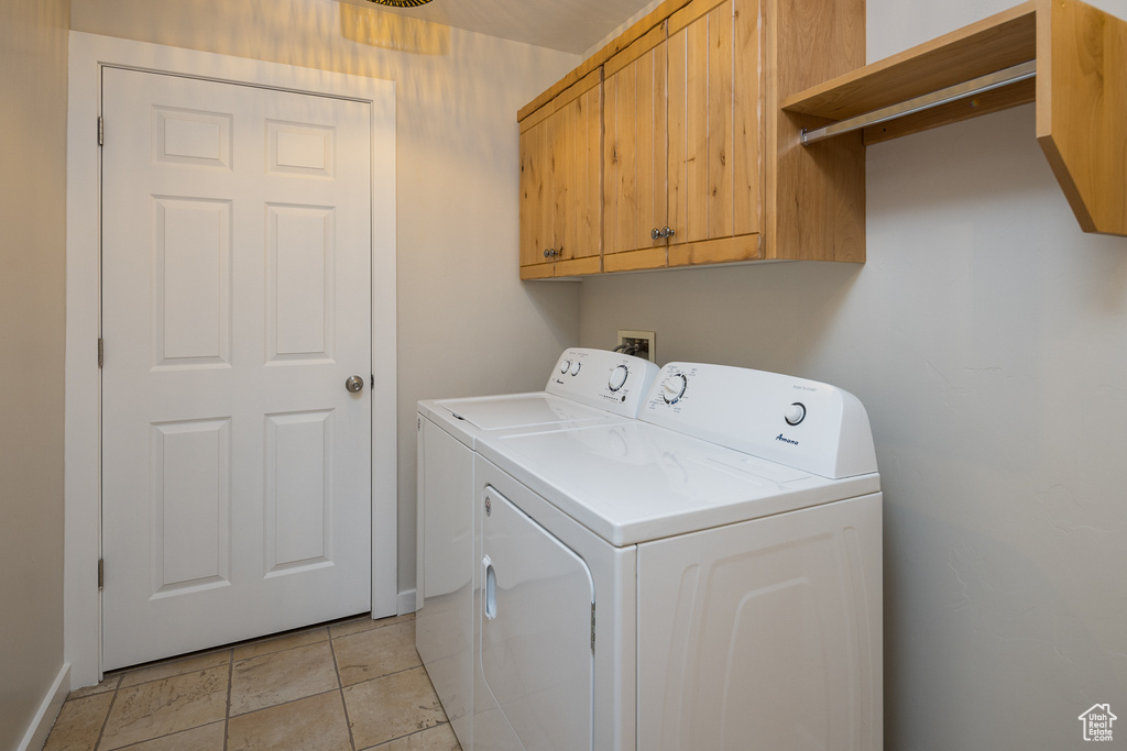 Clothes washing area with light tile patterned floors, cabinet space, and washer and dryer