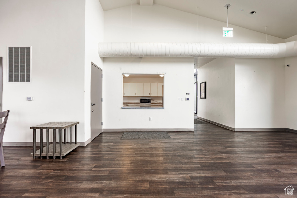 Unfurnished living room with high vaulted ceiling, baseboards, dark wood-style flooring, and visible vents
