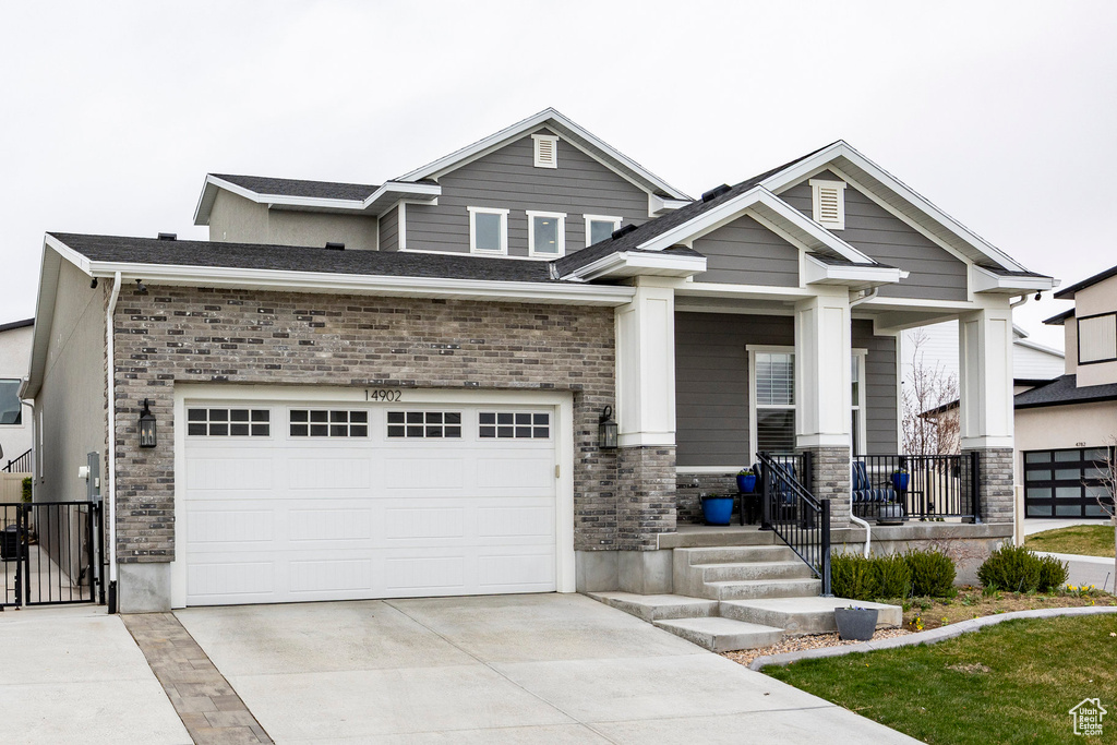 Craftsman-style house with an attached garage, stone siding, a gate, a porch, and driveway