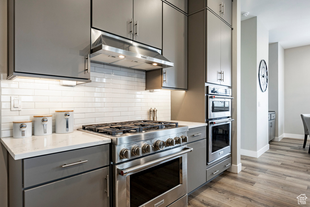 Kitchen with under cabinet range hood, appliances with stainless steel finishes, decorative backsplash, and gray cabinets