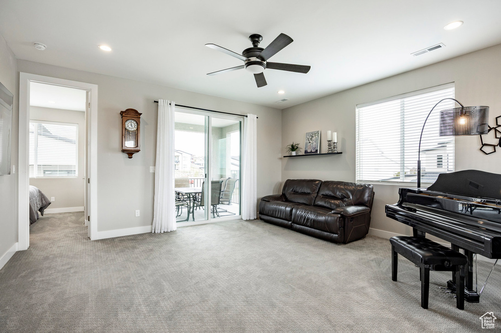 Carpeted living room with ceiling fan, visible vents, and a wealth of natural light