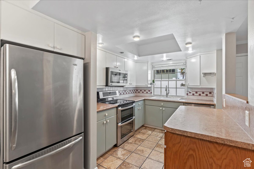 Kitchen with appliances with stainless steel finishes, a sink, backsplash, and white cabinetry