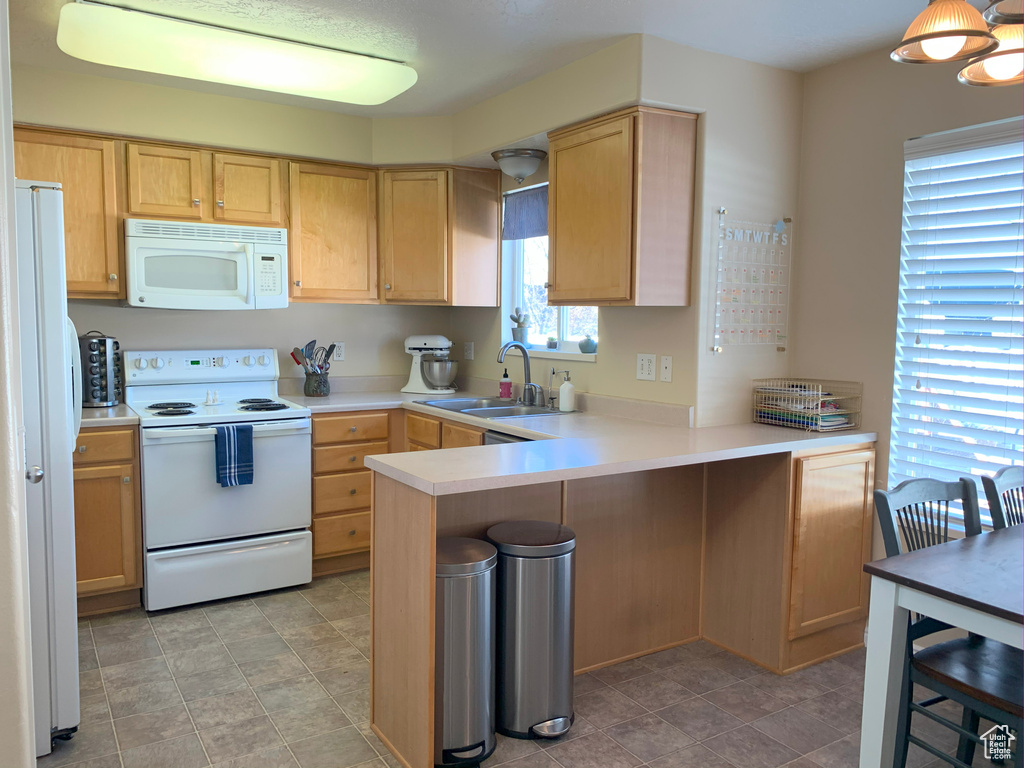 Kitchen with light countertops, a sink, light brown cabinetry, a peninsula, and white appliances