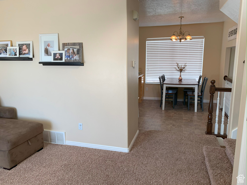 Interior space with carpet flooring, a chandelier, a textured ceiling, baseboards, and visible vents