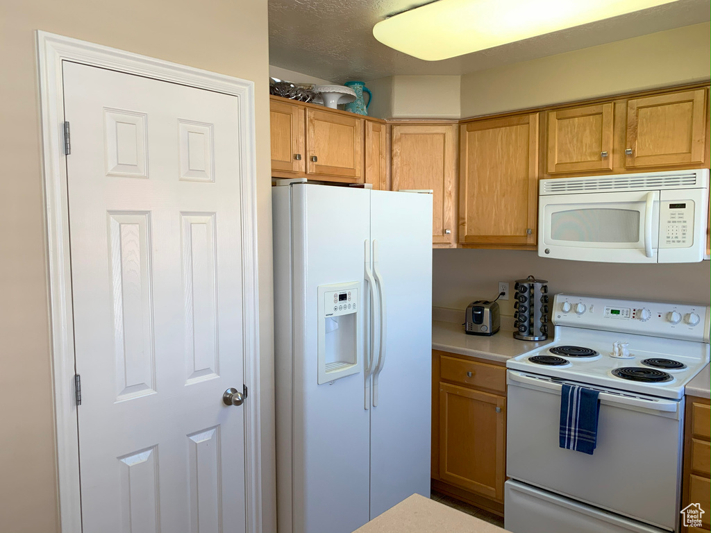 Kitchen with white appliances, light countertops, and brown cabinetry