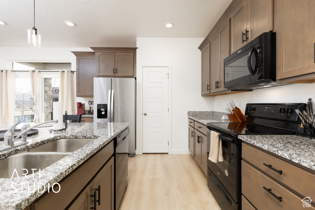 Kitchen featuring a sink, light stone countertops, hanging light fixtures, black appliances, and light wood-style floors