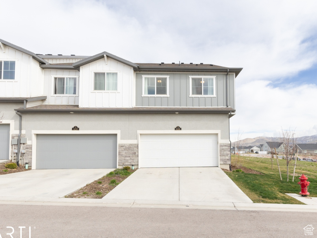 Multi unit property featuring stone siding, an attached garage, central AC, concrete driveway, and a front lawn