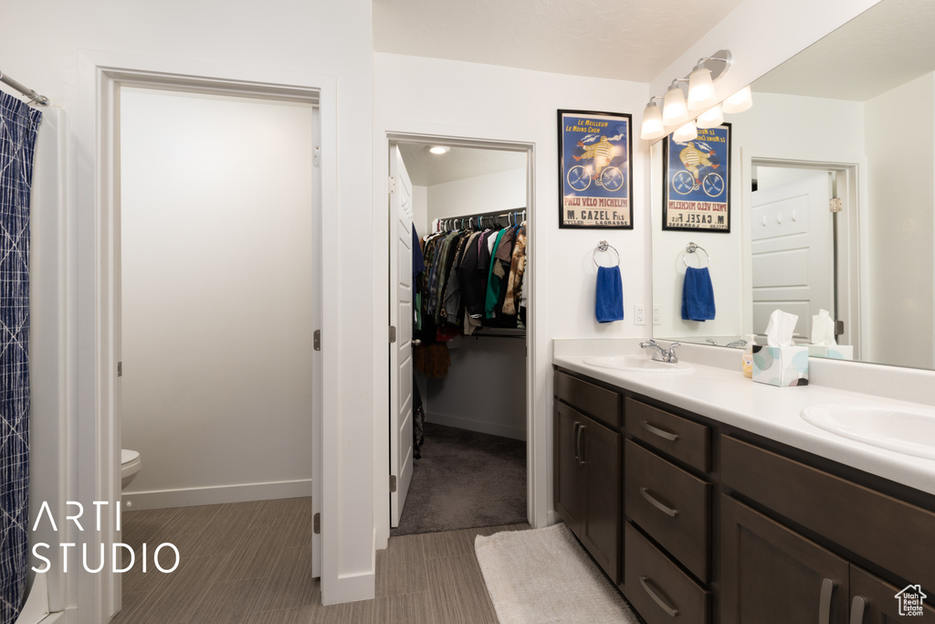 Bathroom featuring double vanity, a sink, toilet, and a spacious closet