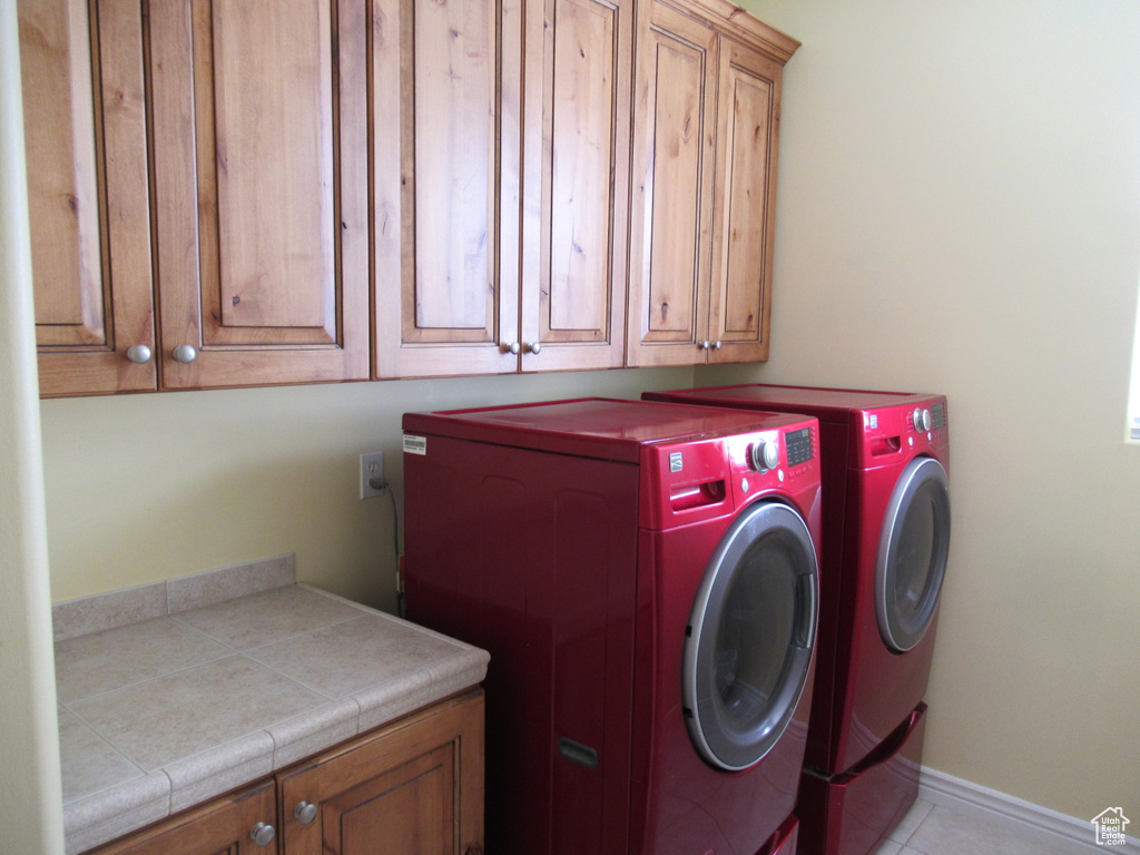 Clothes washing area with baseboards, cabinet space, washing machine and dryer, and light tile patterned floors