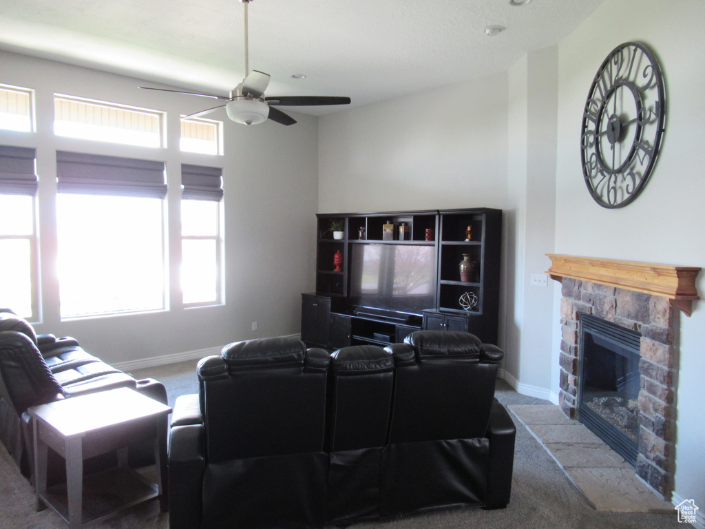 Living room featuring carpet floors, baseboards, a stone fireplace, and ceiling fan