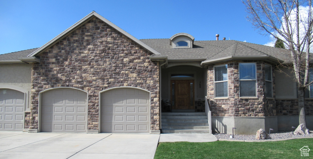 View of front of property with stone siding, a shingled roof, a garage, and concrete driveway