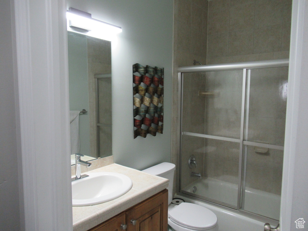 Bathroom with toilet, bath / shower combo with glass door, and vanity
