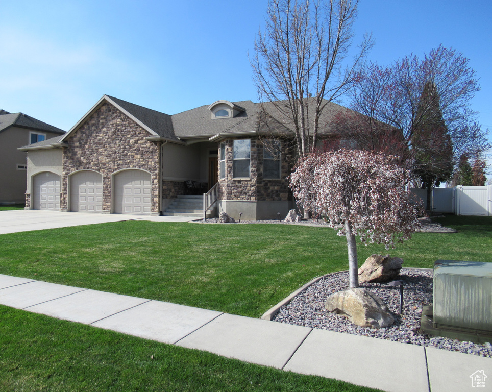 View of front of home with stone siding, concrete driveway, fence, a front lawn, and a garage