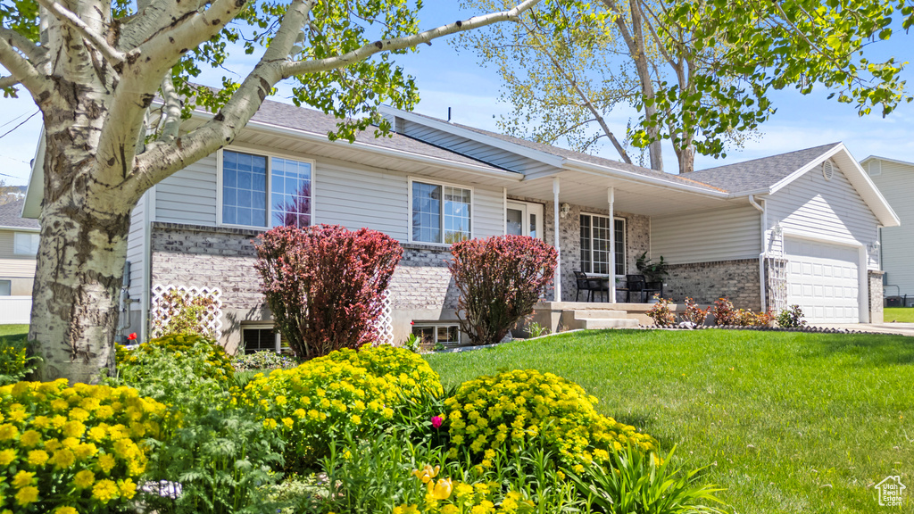 Ranch-style home featuring an attached garage, a front yard, brick siding, covered porch, and a shingled roof