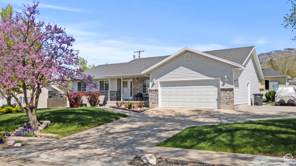 Ranch-style house featuring an attached garage, driveway, a front yard, a shingled roof, and a mountain view