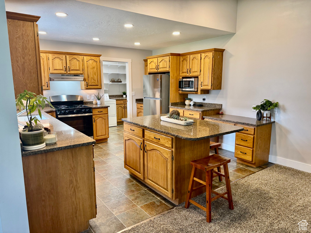 Kitchen with stainless steel appliances, under cabinet range hood, a kitchen island, recessed lighting, and washer / clothes dryer