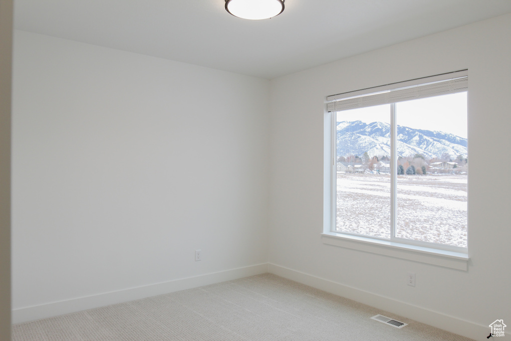 Empty room featuring light carpet, baseboards, a mountain view, and visible vents