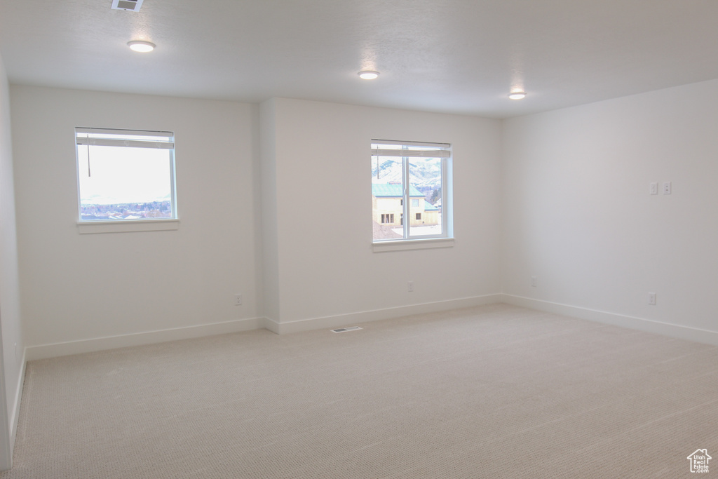 Empty room with baseboards, visible vents, and light carpet