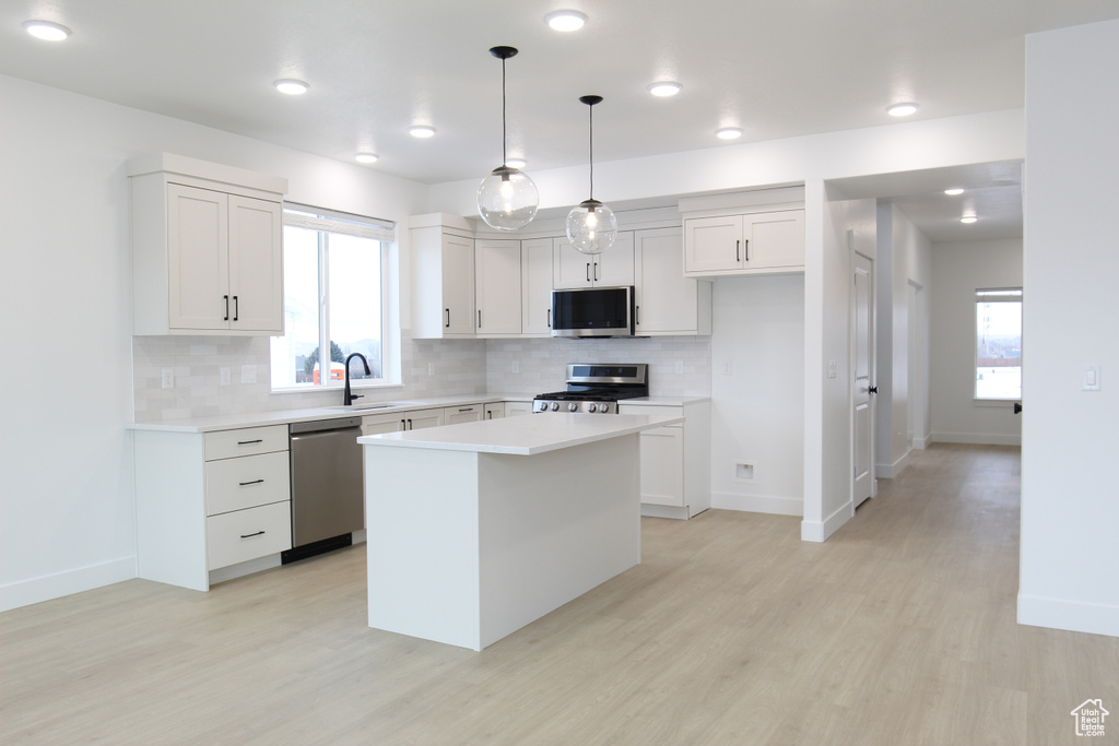Kitchen featuring light countertops, a sink, appliances with stainless steel finishes, light wood-type flooring, and decorative backsplash