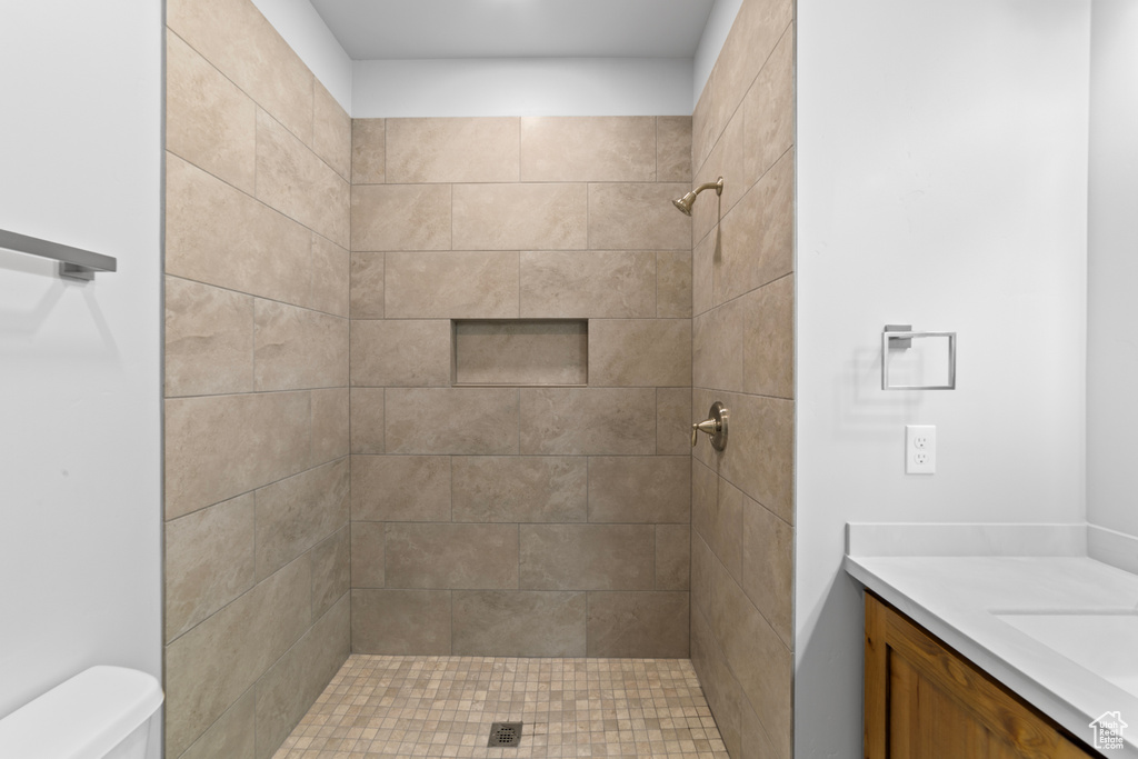 Full bath with toilet, a tile shower, and vanity