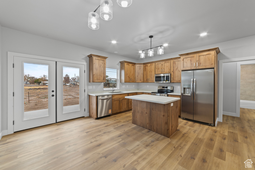 Kitchen with light countertops, light wood finished floors, stainless steel appliances, a kitchen island, and a sink