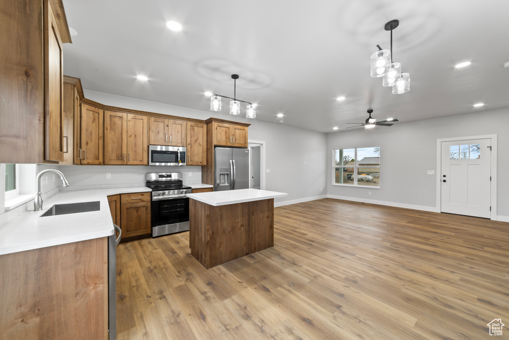 Kitchen featuring decorative light fixtures, stainless steel appliances, a center island, a sink, and brown cabinets
