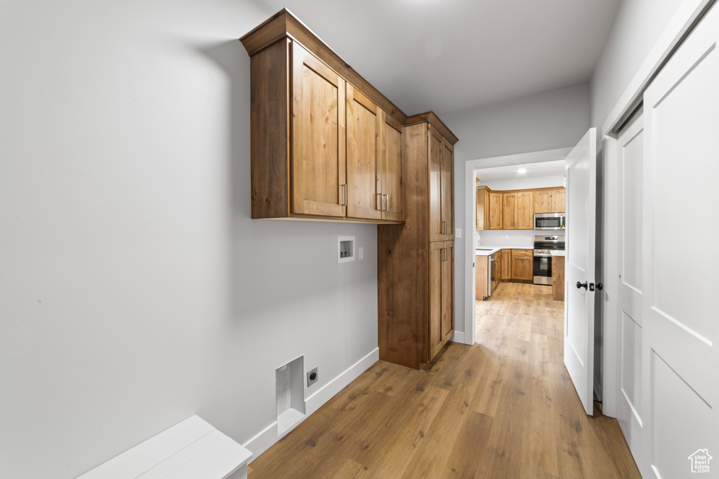 Clothes washing area featuring baseboards, cabinet space, light wood finished floors, electric dryer hookup, and washer hookup