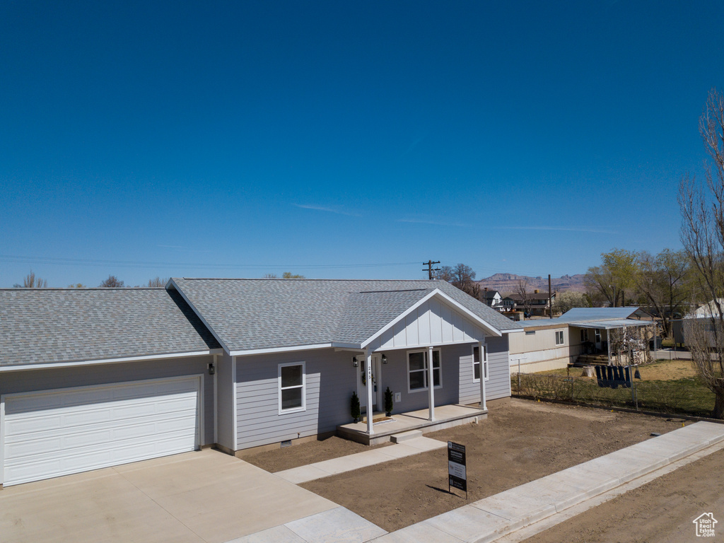 View of front of property with an attached garage, covered porch, board and batten siding, concrete driveway, and roof with shingles