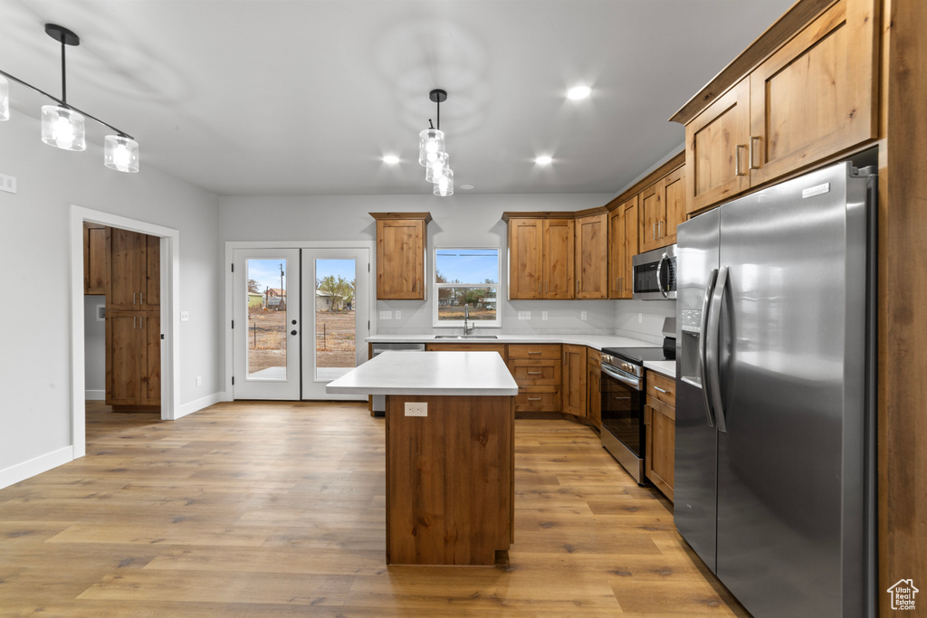 Kitchen featuring light countertops, a sink, a kitchen island, light wood finished floors, and appliances with stainless steel finishes
