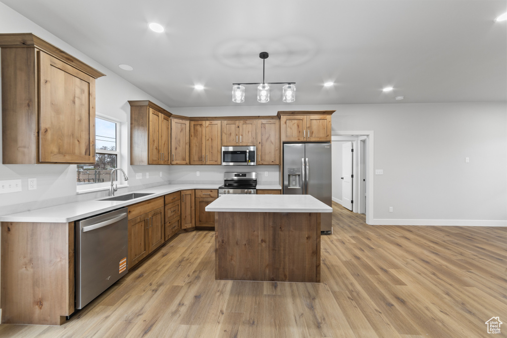 Kitchen featuring light countertops, light wood-style flooring, appliances with stainless steel finishes, a sink, and a center island
