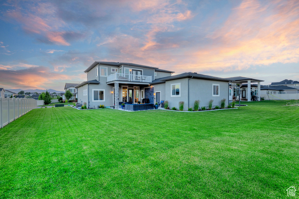 Rear view of house featuring a patio area, stucco siding, fence, a balcony, and a lawn
