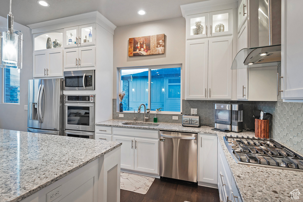 Kitchen featuring backsplash, a sink, stainless steel appliances, wall chimney range hood, and white cabinets