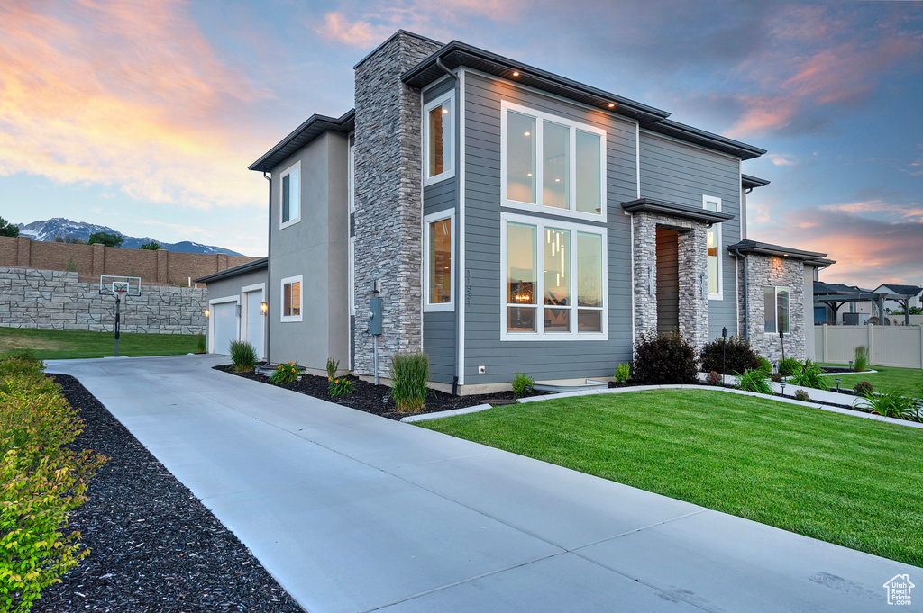 View of side of home featuring concrete driveway, fence, stone siding, a garage, and a lawn