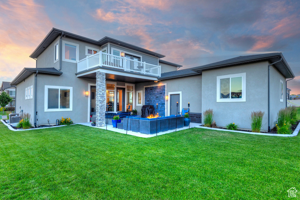 Back of house featuring stucco siding, cooling unit, a balcony, a patio, and a lawn