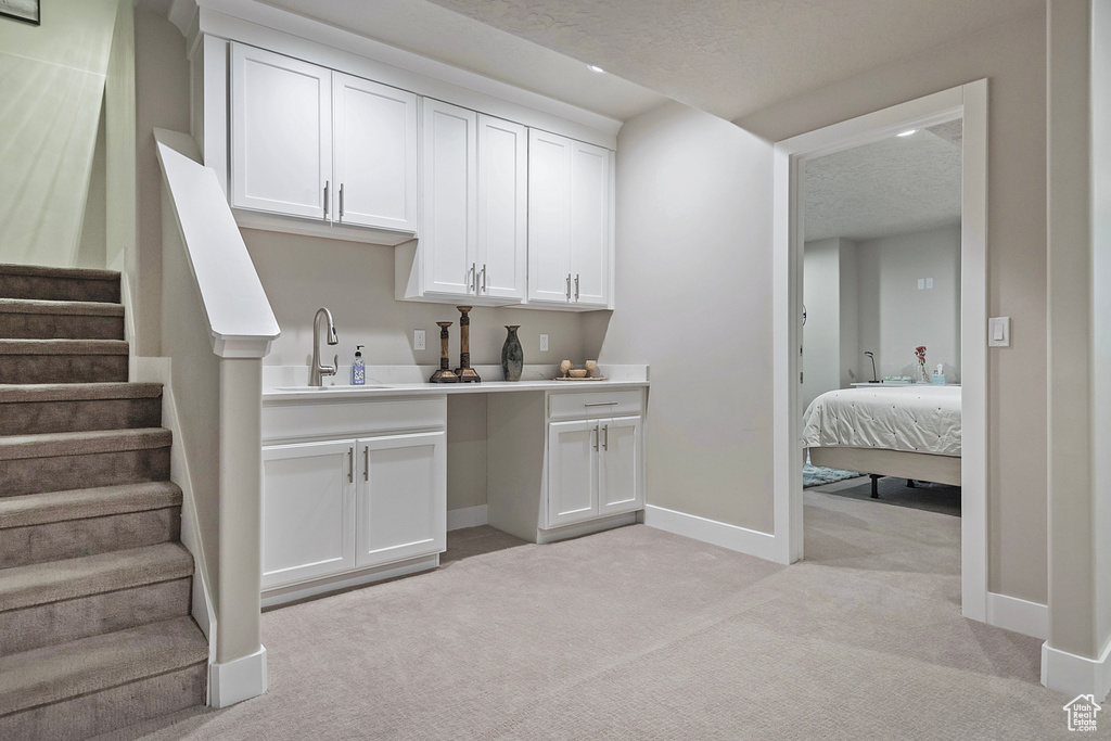 Kitchen with baseboards, a textured ceiling, a sink, white cabinets, and light carpet