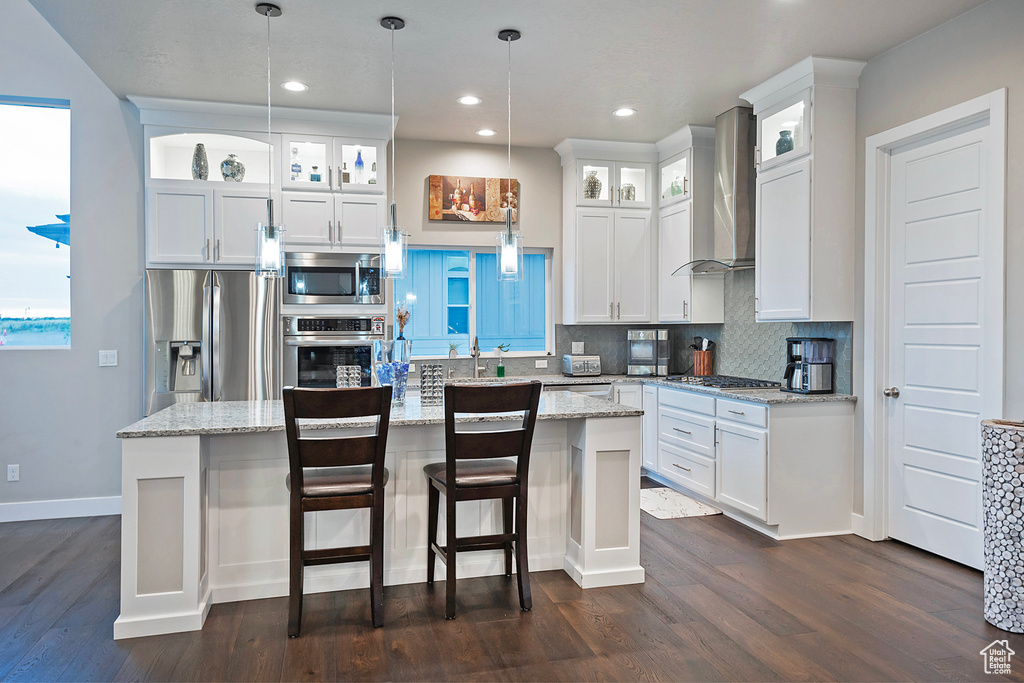 Kitchen featuring wall chimney range hood, dark wood-style flooring, appliances with stainless steel finishes, and decorative backsplash