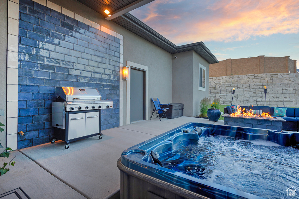Patio terrace at dusk with an outdoor fire pit, grilling area, fence, and a hot tub