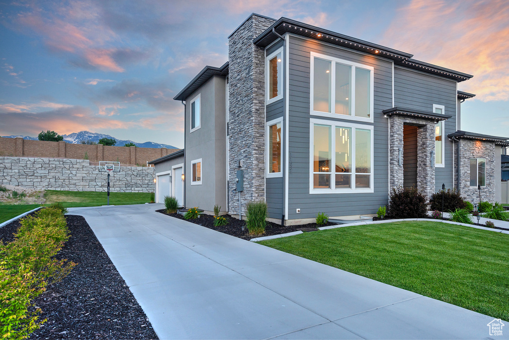 Exterior space with stone siding, fence, concrete driveway, a front yard, and a mountain view