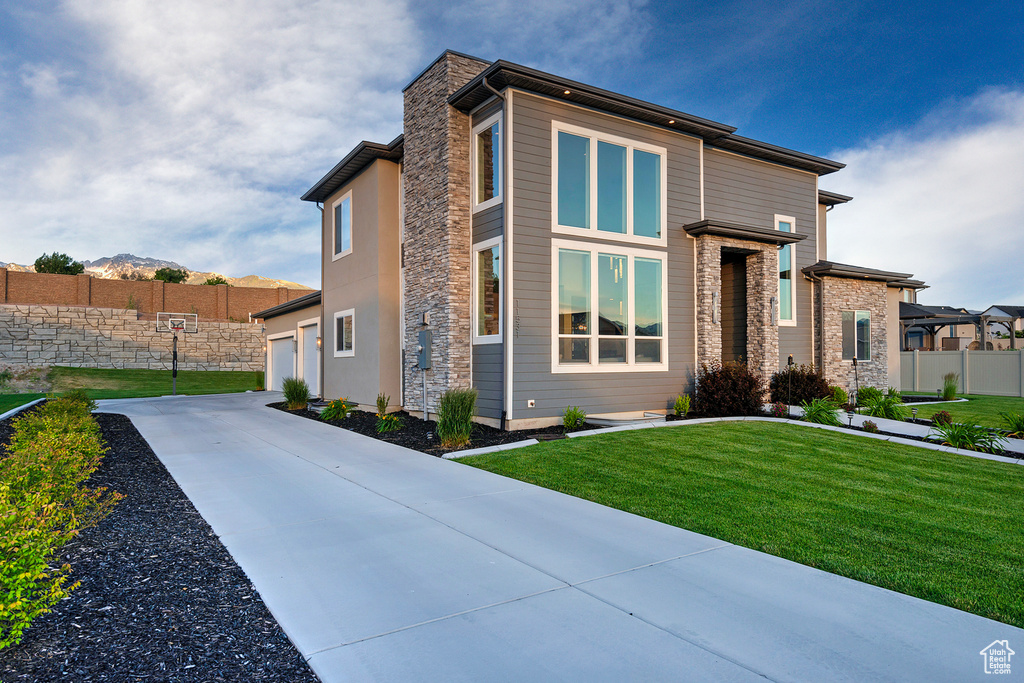 View of front of property with concrete driveway, fence, stone siding, a front lawn, and a garage