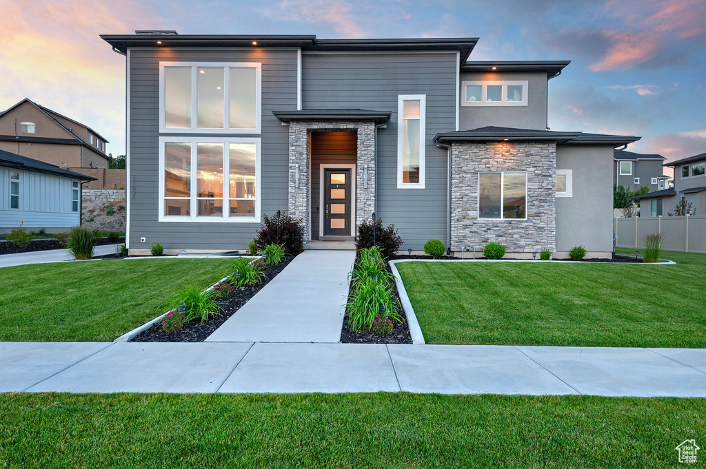 Contemporary home featuring stone siding, fence, and a yard