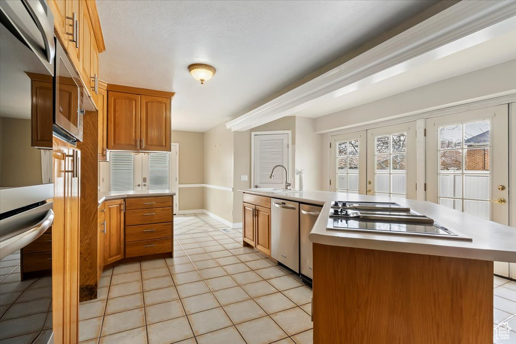 Kitchen featuring light countertops, a sink, stainless steel dishwasher, black electric stovetop, and light tile patterned floors
