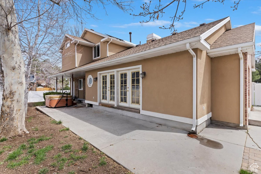 Rear view of property featuring stucco siding, a hot tub, french doors, a patio area, and a chimney