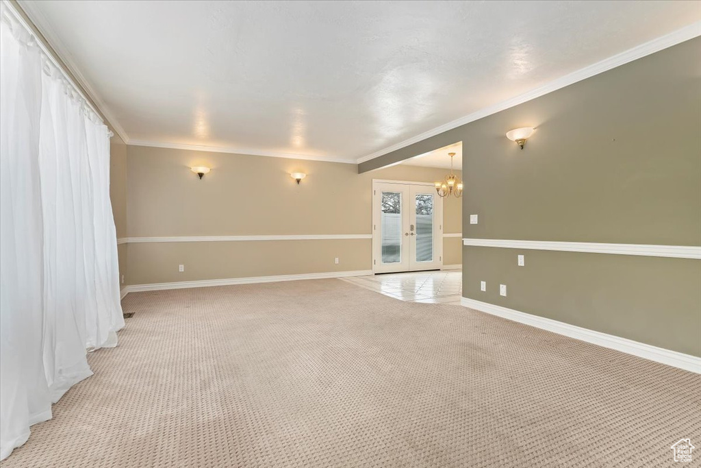 Unfurnished room featuring french doors, an inviting chandelier, ornamental molding, baseboards, and light carpet