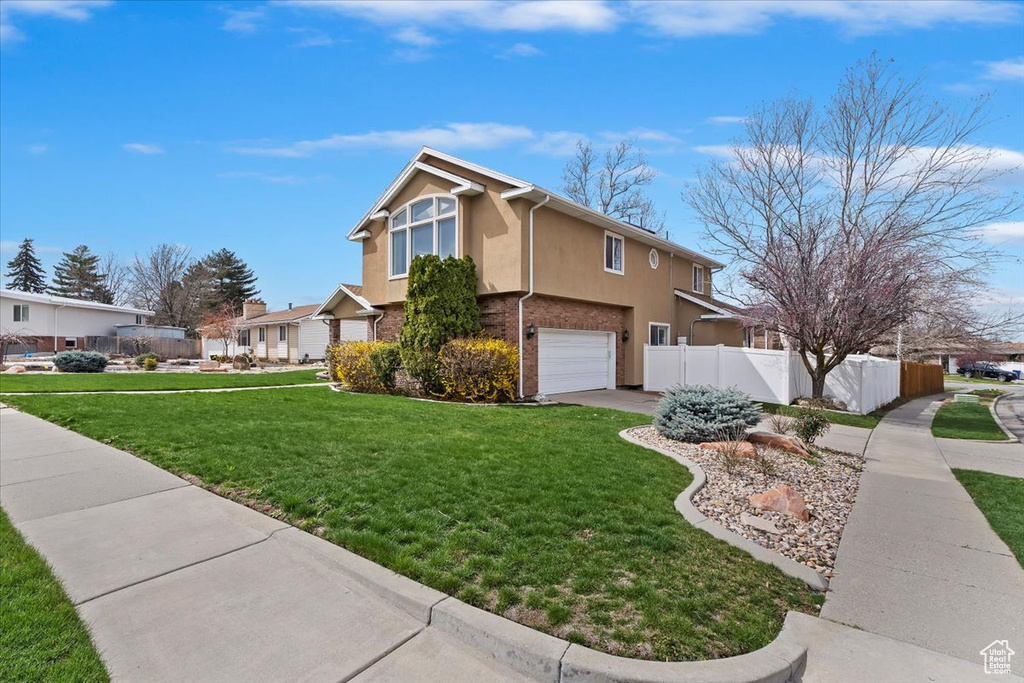 View of side of property featuring stucco siding, fence, an attached garage, driveway, and a lawn