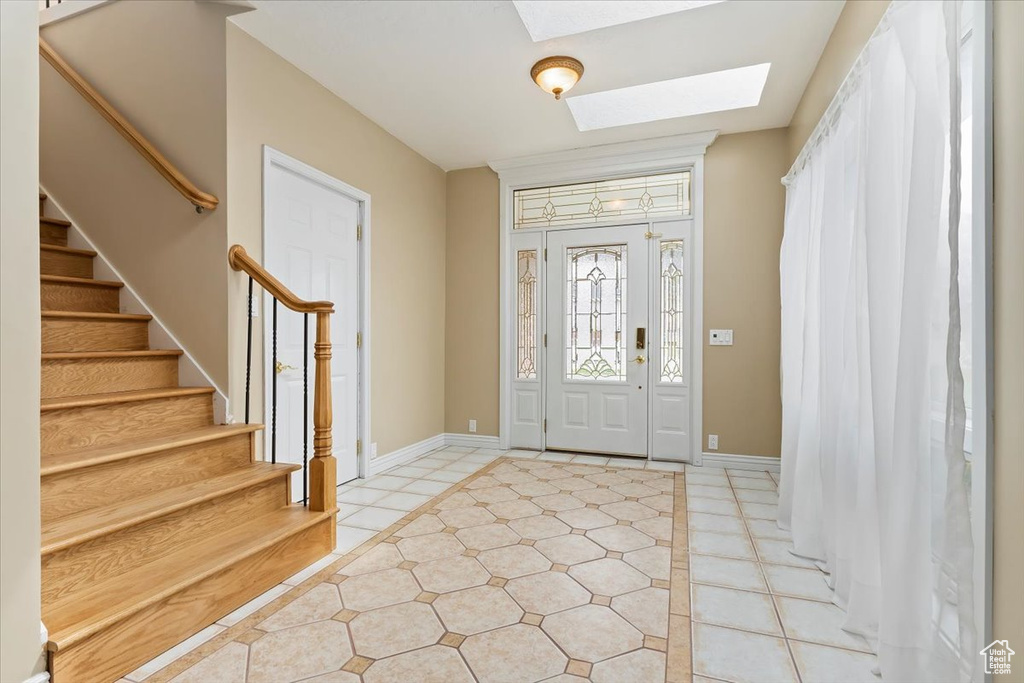 Foyer entrance with light tile patterned floors, a skylight, stairway, and baseboards