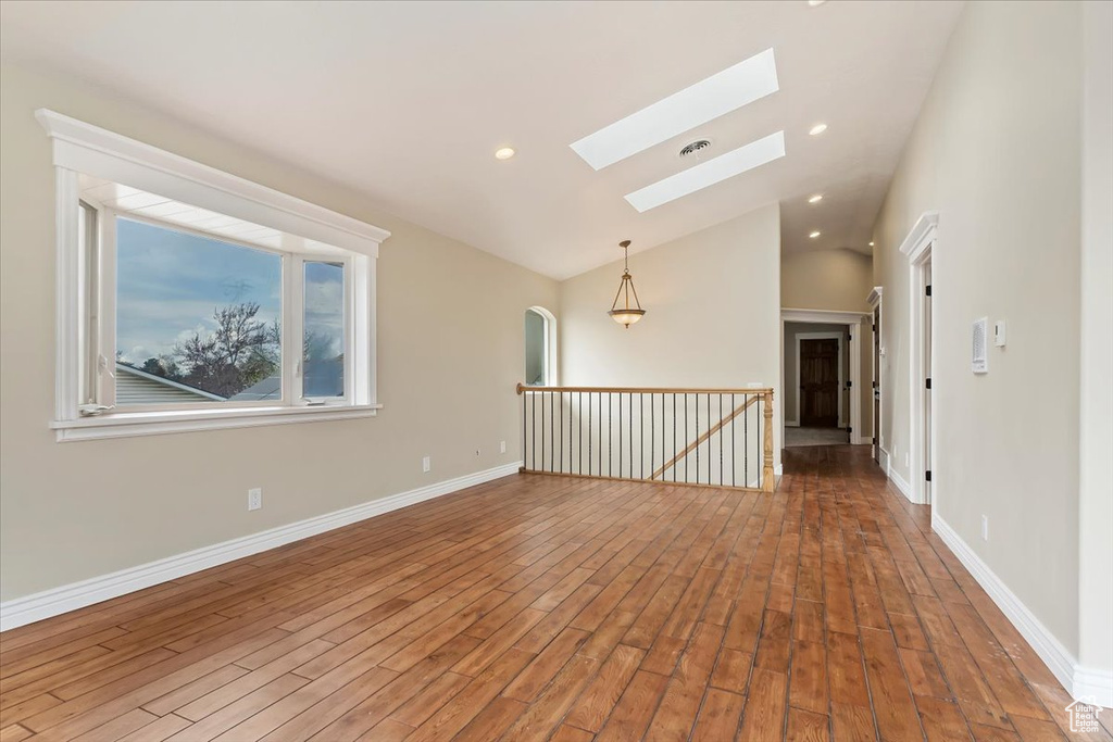 Empty room featuring baseboards, wood finished floors, lofted ceiling with skylight, and recessed lighting