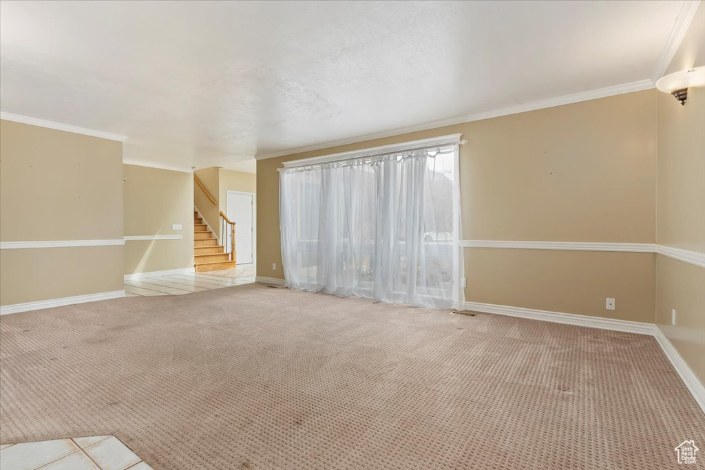 Unfurnished living room featuring ornamental molding, carpet, baseboards, and stairway