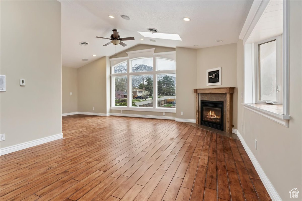 Unfurnished living room with wood finished floors, a glass covered fireplace, baseboards, visible vents, and lofted ceiling with skylight