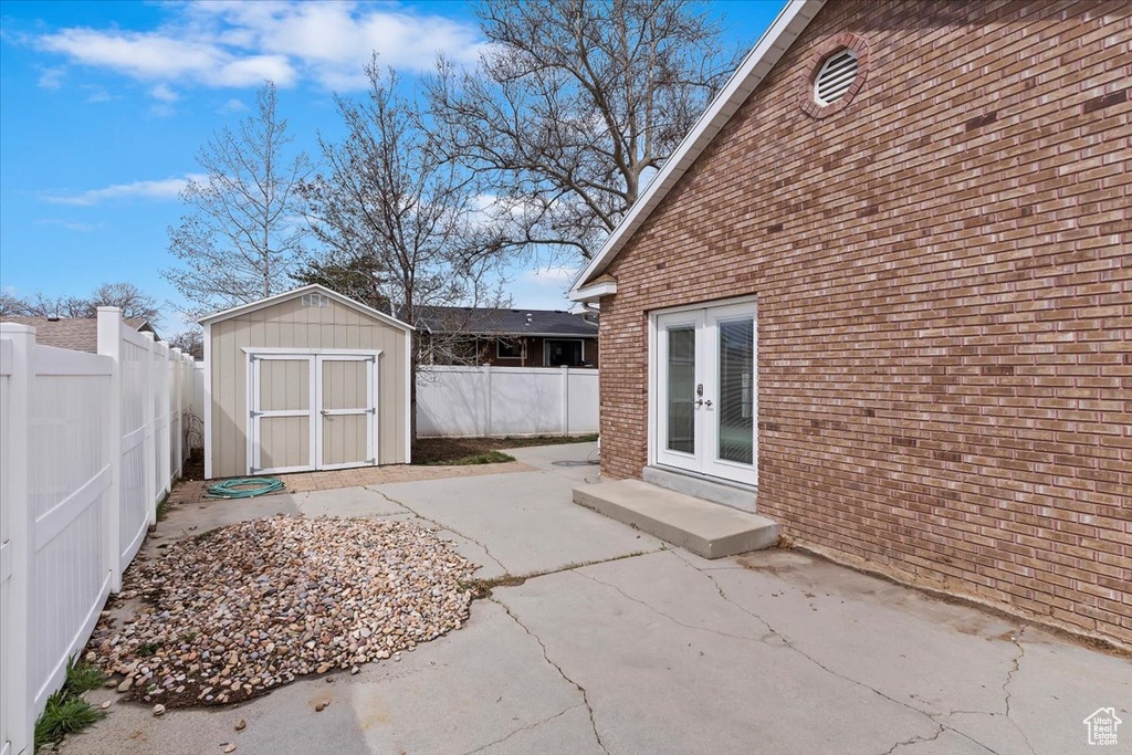 View of patio featuring french doors, a fenced backyard, an outdoor structure, and a storage shed